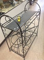 Full view of the wrought iron stand showing decorative scrollwork on the sides and three flat shelves, with measuring tape on top.