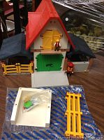 Playmobil farm set showing barn with red roof, figures on and around barn, yellow fence piece, and accessories on white base.