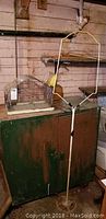 Photo of wire birdcage on table and vintage metal birdcage stand positioned in front of a rustic wall and green cabinet