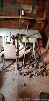 Full view of vintage wooden wheelbarrow, metal wheel, and assortment of hand tools arranged on floor next to workbench.