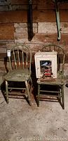 Two vintage green-painted wooden chairs against rustic wood wall, one chair holds tin medicine cabinet with mirror and vintage iron on seat.