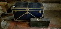 Photo showing metal steamer trunk and vintage suitcase on floor in dim environment