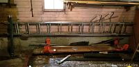 Photo shows a long metal extension ladder mounted on the wall, and the work bench's wooden surface with orange adjustable leg brackets underneath.