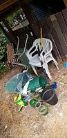 Photo showing plastic fencing roll, two white plastic patio chairs, assorted glass pots, hand pruners, small garden tools, and other containers on ground.