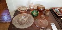 Full lot of vintage glassware including vases, plates, candy dish and decorative glass pieces arranged on a table.