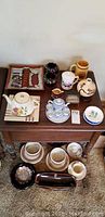 Overview of assorted pottery bowls, ceramic vases, ashtrays including a rectangular ashtray and floral painted ceramic pieces arranged on a wooden table and lower shelf