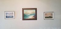 Three framed artworks hanging on a wall: center is a large oil painting of an ocean scene, flanked by two smaller nautical prints.
