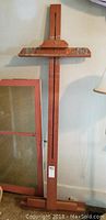 Full view of wooden easel standing against wall with adjacent window frame visible.