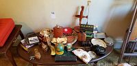 Wide view of the table containing the wooden statue, vintage binoculars, brass alligator nutcracker, vintage drawing instruments, coasters, and other assorted items.