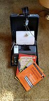Smith Corona typewriter inside open black carrying case with paper loaded and instruction books in front