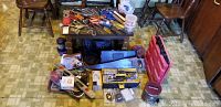 Overall view of all items arranged on a table and floor - hand tools, hand saws, toolbox, hardware, level, locks, and light bulbs visible