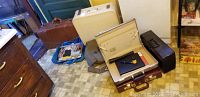 Photo showing multiple vintage suitcases and briefcases arranged on floor including white, brown, beige suitcases and others.