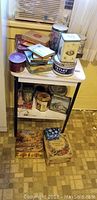 Full view of the metal table with various collectible tins stacked on and beneath it, showing a variety of sizes and themes.