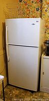 Full front view of white top freezer Maytag refrigerator with visible handles and surrounding kitchen area.