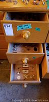 Three open wooden dresser drawers filled with assorted costume jewellery including rings, pins, watches, and earrings.