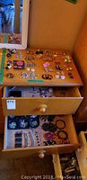 Top view of wooden drawer with multiple earrings arranged on the surface and inside opened drawers showing bracelets and more earrings.