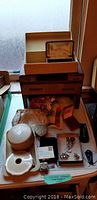 Overview of lot items including vintage metal compact with mirror, wooden jewelry box with drawers, small trinket boxes, vintage evening bag, jewelry pieces, and ceramic dishes.