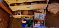 Sewing supplies including open wicker sewing basket filled with thread spools and notions, alongside two small cases containing yarn and additional supplies, with drawers above them partially open to reveal more sewing supplies.