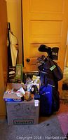 Overview of the golf bag, boxes with golf accessories, gloves, balls, and books stacked by a door.