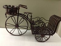 Full side view of the dark brown metal decorative bicycle plant holder showing the overall shape and structure with front and rear baskets.