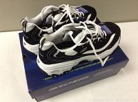 Pair of new black and white Skechers men's athletic shoes on top of the original Skechers blue box, showing memory foam label on tongue and white laces.