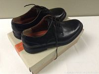 Pair of men's black leather dress shoes placed on top of the original Clarks shoe box with an orange band and logo.