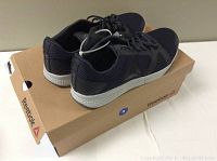 Black men's Reebok shoes on top of Reebok shoe box showing style and design detail.