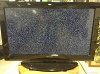 Front of Toshiba 32 inch TV displaying static screen with black glossy bezel and stand.