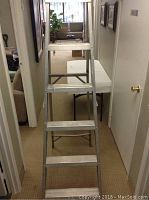 Front view of a silver 6-foot aluminum step ladder with five steps and cross bracing in an indoor hallway.
