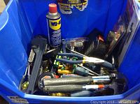 Blue bin filled with miscellaneous hand tools including screwdrivers, pliers, WD-40 spray can, and other tools.