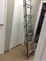 Photos showing a lightweight aluminum extension ladder standing upright indoors. Ladder is fully assembled in both photos, showing front and side views with visible locking mechanisms.