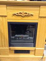 Front view of the wooden mantel and electric fireplace insert with black framing and carved detail.