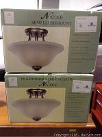 Two boxed semi flushmount light fixtures branded Nicole, showing antique bronze finish and etched glass shades on packaging.