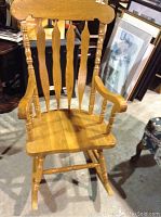 Front view of solid wood rocking chair with natural finish, showing spindled back and contoured seat.