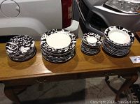 Photo showing four stacks of plates and bowls on a wooden table, all featuring a black and white swirl pattern on the rims.