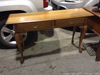 Wooden hall or sofa table with two drawers, curved legs, and medium wood finish shown in a warehouse setting.