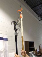 Photo showing two tree limb cutters with different colored cutting heads and poles, held upright indoors against a wall.