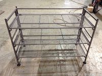 Metal shoe rack with three mesh shelves and black finish photographed on concrete floor.