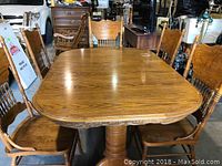 Full view of oak dining table with five chairs arranged around it.