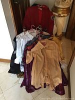 A collection of clothing on hangers piled by the wall including a red Georgia Bulldogs sport coat and various blouses beneath it.