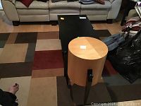 Photo showing a rectangular black coffee table with two drawers and bottom shelf and a round wood table on a geometric patterned area rug.
