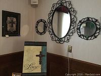 Overall view of the decorative wall mirrors, wall art with cross, and metal artwork with easel hanging on wall.