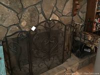 Full view of decorative metal fireplace screen centered on stone hearth with ornate scroll pattern