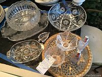 Photo showing multiple crystal candy dishes, cut glass punch bowl, salt and pepper shakers, serving bowl and trays with etched floral and starburst patterns.