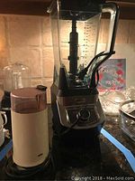 Photo shows a black Ninja blender with large clear pitcher, stainless steel accents, and next to it a white Braun coffee grinder with clear lid containing coffee ground residue.