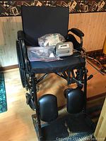 Black Probasics wheelchair with attached nebulizer and accessories on seat, placed on wooden floor.