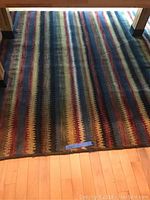 Large striped rug with colorful horizontal zigzag stripes on wood floor under a table.