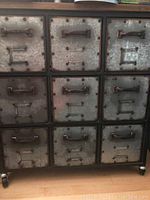 Front view showing three-by-three grid of galvanized steel drawers in black iron frame with wooden top and casters