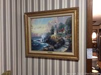 Full frontal view of Thomas Kinkade framed wall art hung on striped wallpaper
