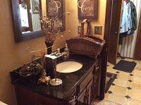 Photo of bathroom counter showing gold-tone freestanding towel holder and rectangular woven wicker magazine rack on black granite countertop